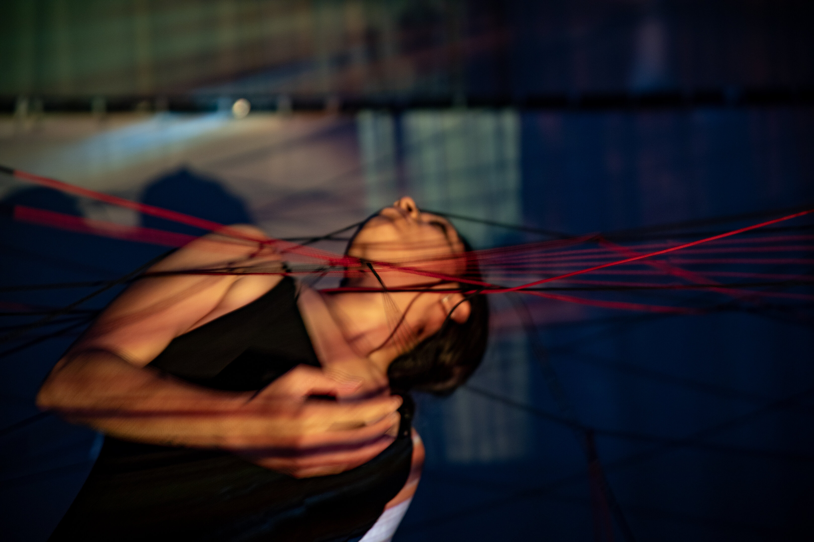 Partially blurry photograph of Priyakshi Agarwal in motion touching a net made out of stretched yarn with her upper body and face.  