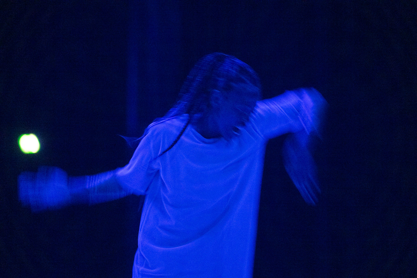 Eine Frau in blauem Licht macht eine schnelle Tanzbewegung mit geöffnetem Mund