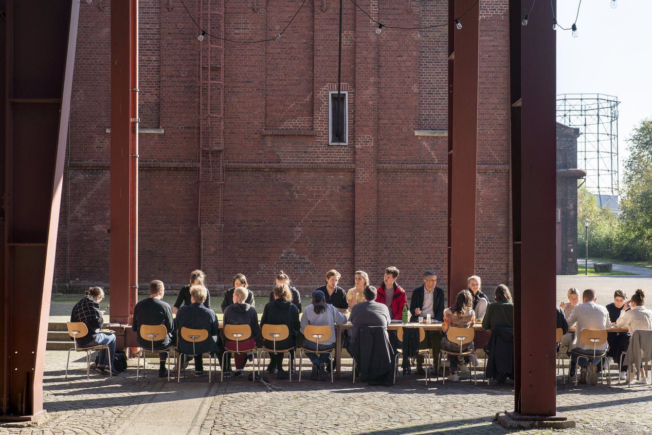 Eine Gruppe Menschen sitzt an einem langen Tisch vor PACT Zollverein