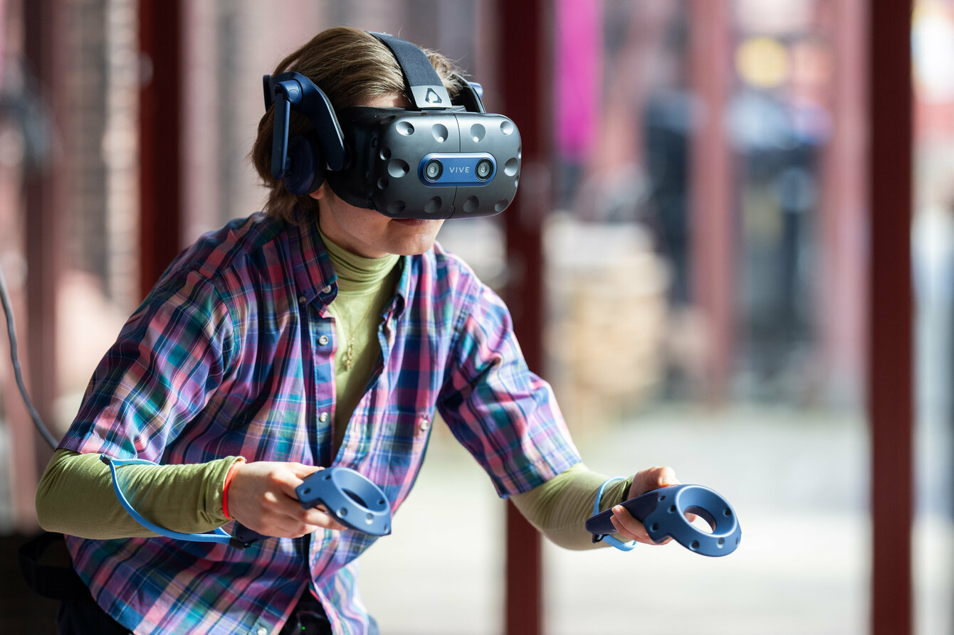 Eine Person hat eine VR-Brille aufgesetzt und hält zwei Controller in der Hand. 