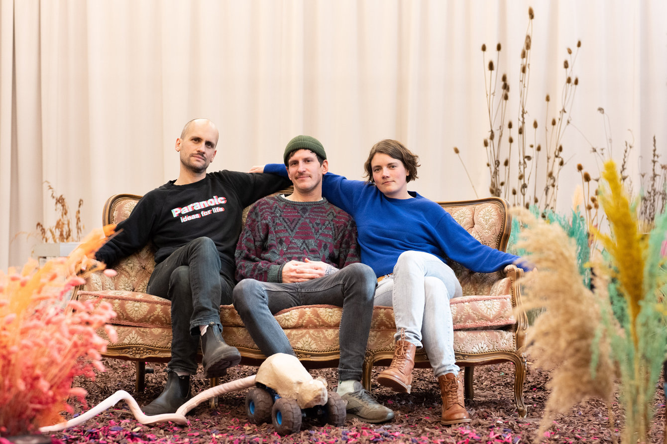 Daniel Ernesto Müller, Simon Hartmann sitzen auf einem Sofa in ihrem Bühnenbild bestehend aus bunten Trockenpflanzen, in ihrer Residenz im PACT Studio 