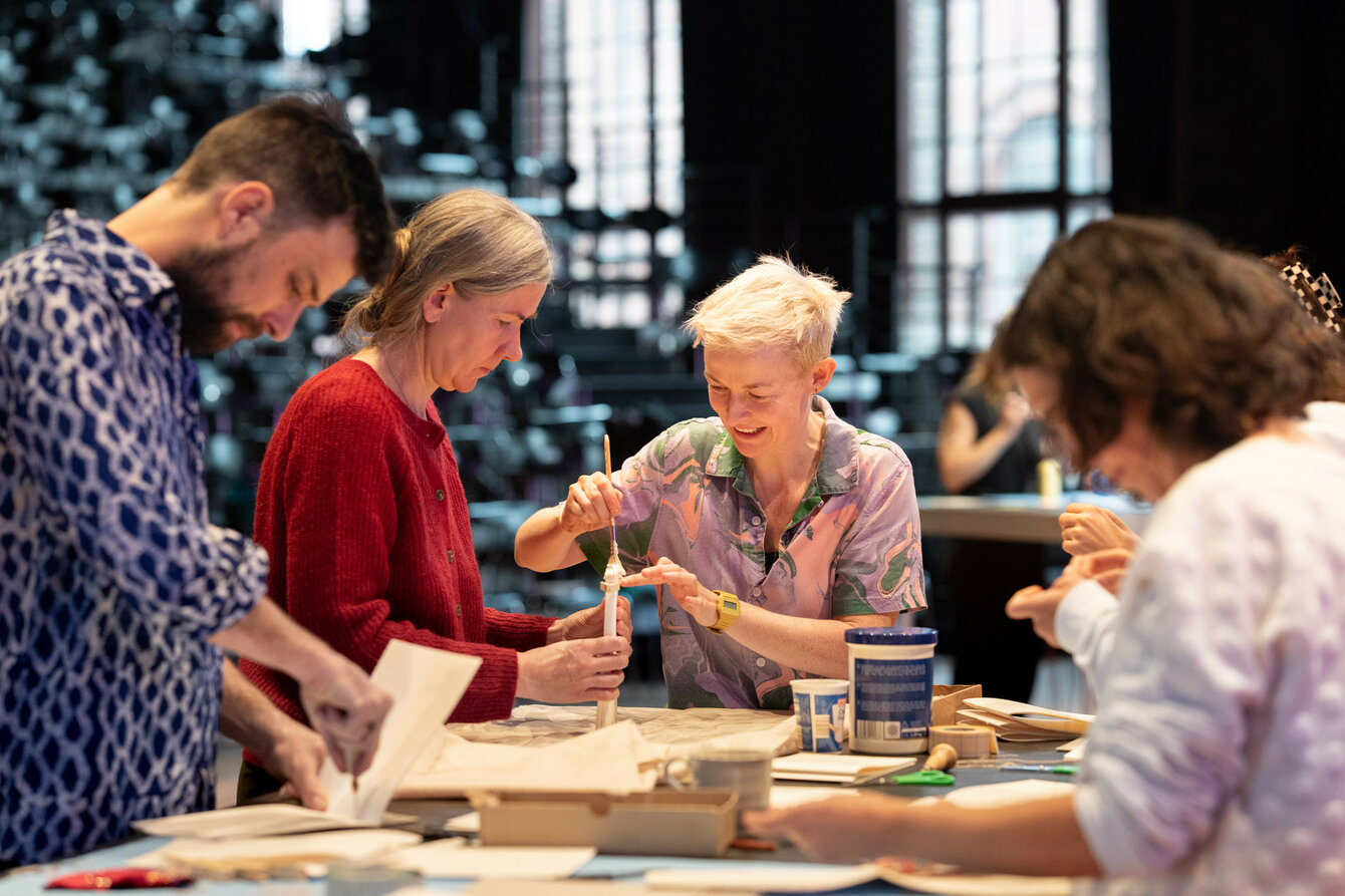 Four people sit together at a table. They are gluing in book spines. The atmosphere is cheerful.