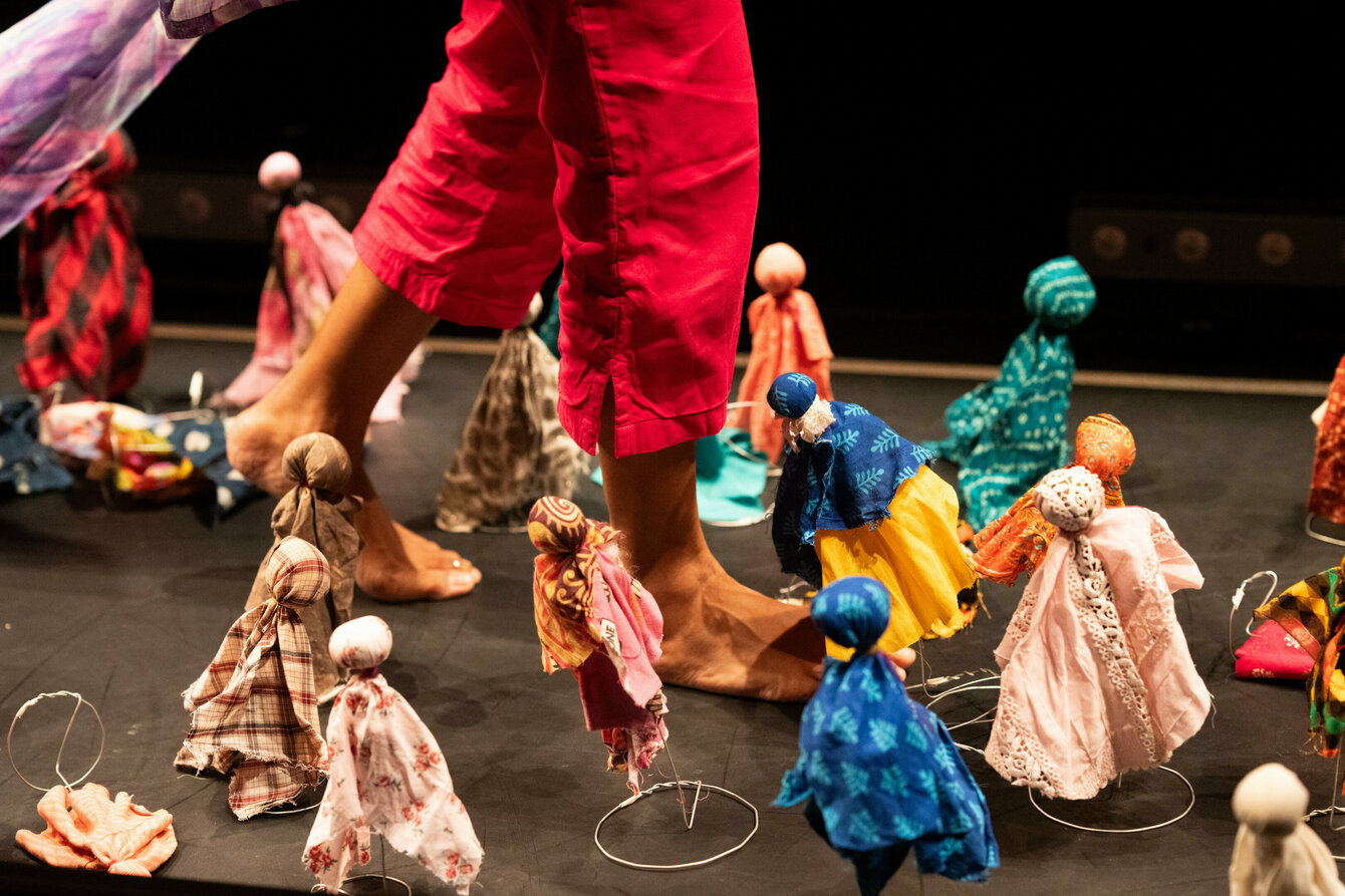 A person walks between many small colorful puppets on the stage floor.