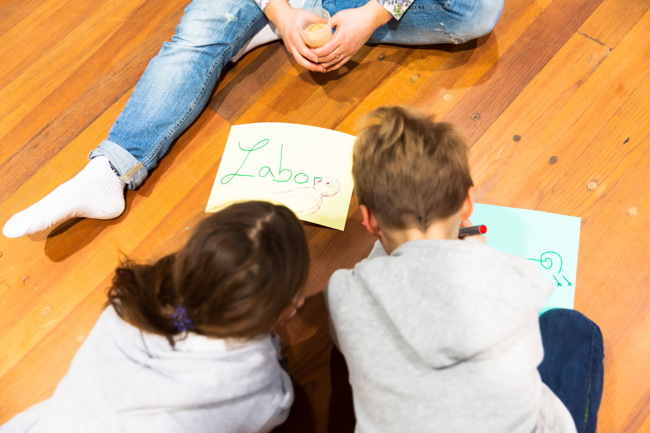 Workshop zu Tanz, Kinder sitzen auf dem Boden und schreiben Begriffe auf Papier