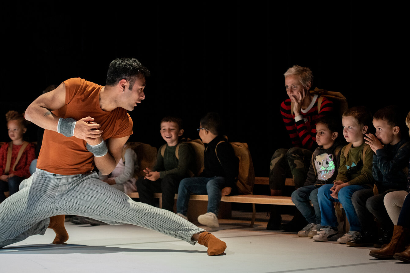 Eine Person macht akrobatische Bewegungen auf dem Boden, Kinder sitzen im Publikum und schauen zu
