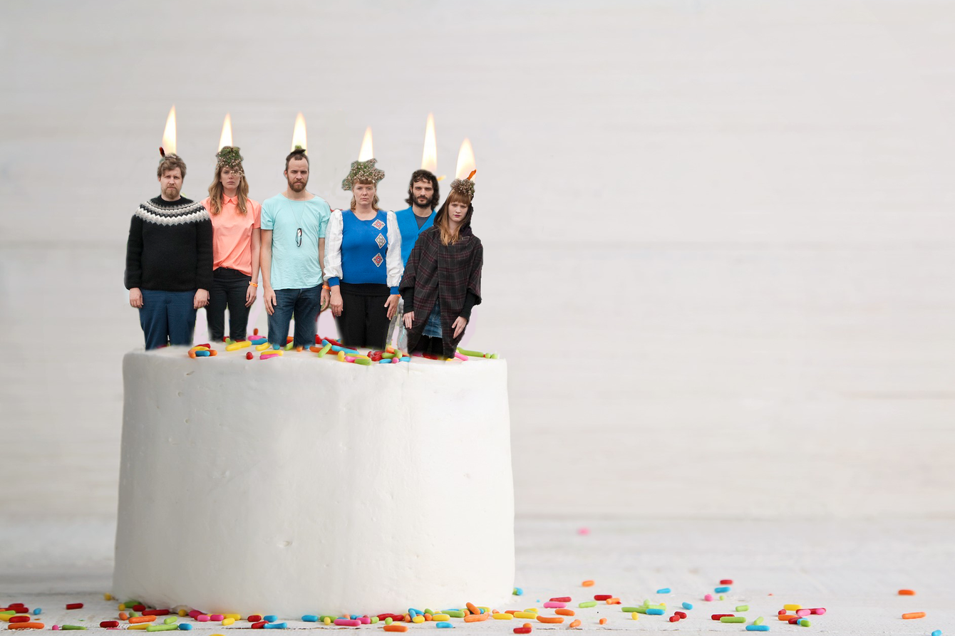 Sechs Bandmitglieder stehen wie Kerzen auf einer Torte, die Köpfe in Flammen.