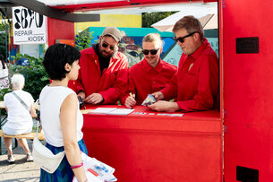 Personen in roten Overalls stehen an einem Kiosk