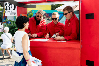 Personen in roten Overalls stehen an einem Kiosk