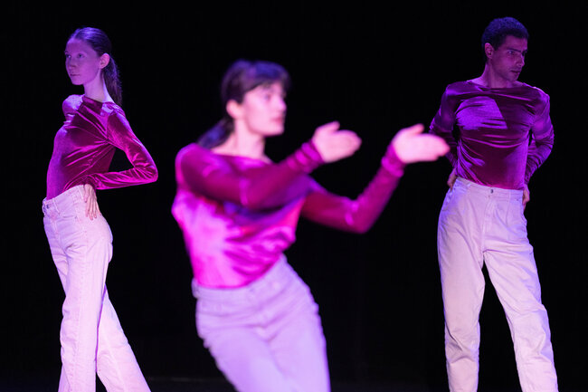 Drei Tänzer:innen in Lila Kleidung auf der Bühne