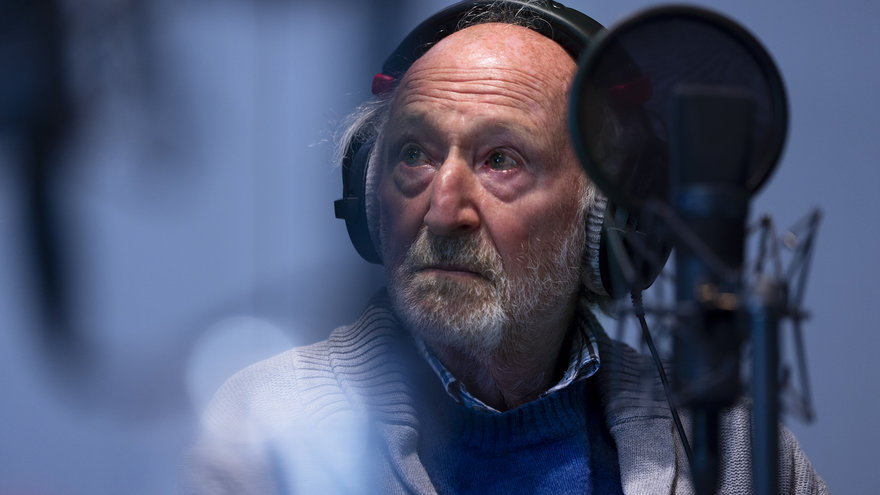 Ein älterer Herr mit Kopfhörern sitzt vor einem Mikro in einem Tonstudio und schaut auf einen nicht sichtbare Person