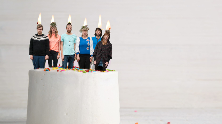 Sechs Bandmitglieder stehen wie Kerzen auf einer Torte, die Köpfe in Flammen.